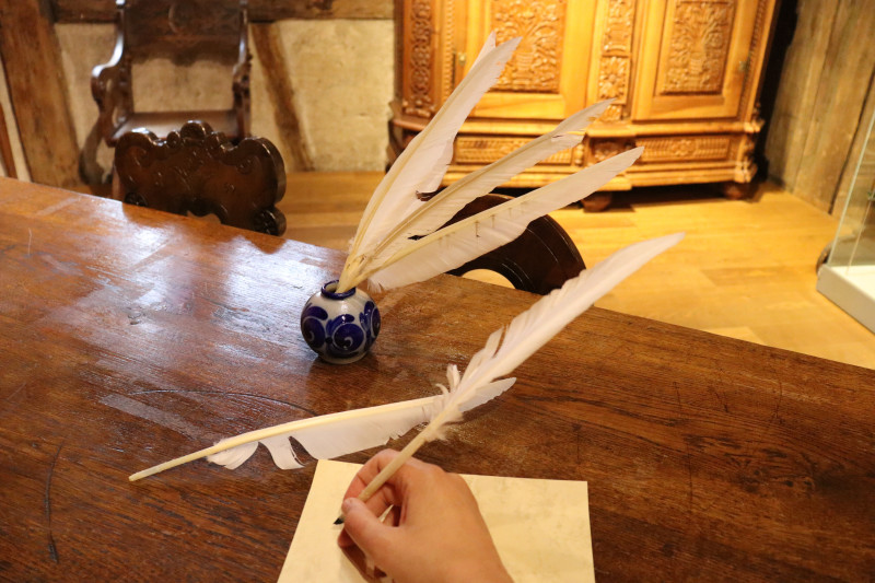 Federkiel Schreiben: Hand schreibt mit Feder auf Papier, Tintenfass und antiker Tisch.