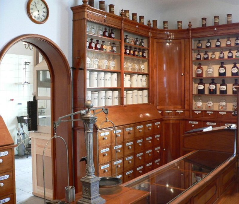 Historische Apotheken-Einrichtung mit Holzregalen, Apothekergläsern, Waage und Verkaufstheke im klassischen Stil.